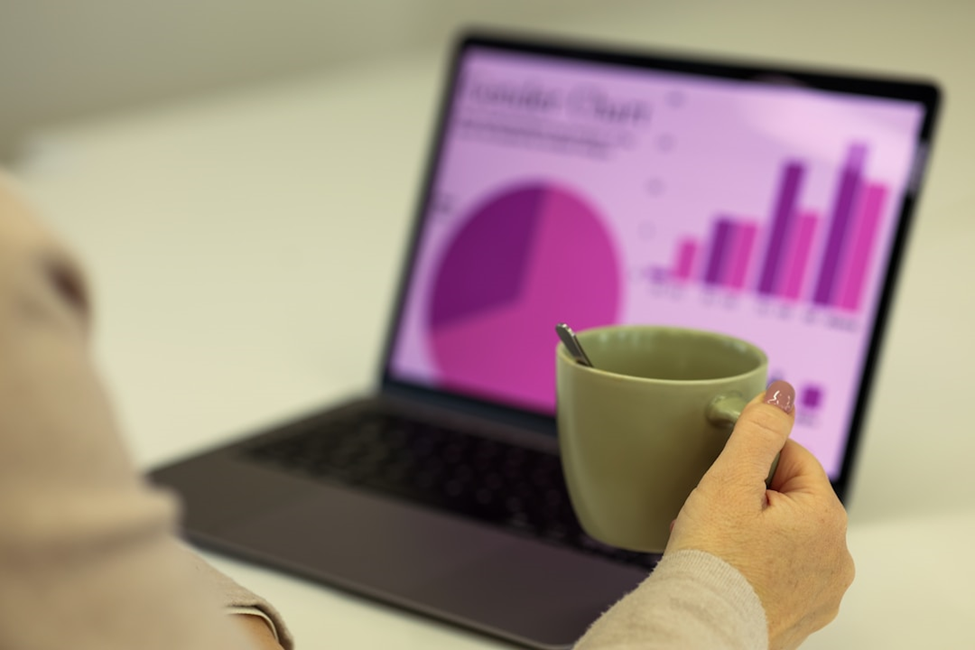 Woman sitting with a mug in hand, in front of a laptop showing pie chart and bar graphs with email marketing for publishers data